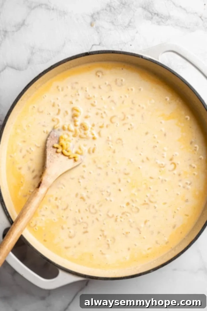 Elbow macaroni simmering gently in a rich, creamy vegan sauce within a skillet, absorbing flavor and thickening as it cooks.