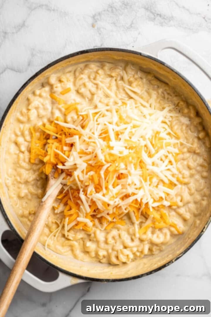 Shredded vegan cheese melting into the hot pasta and sauce in a skillet, creating a gooey, irresistible texture for the 3-Cheese Vegan Mac and Cheese.