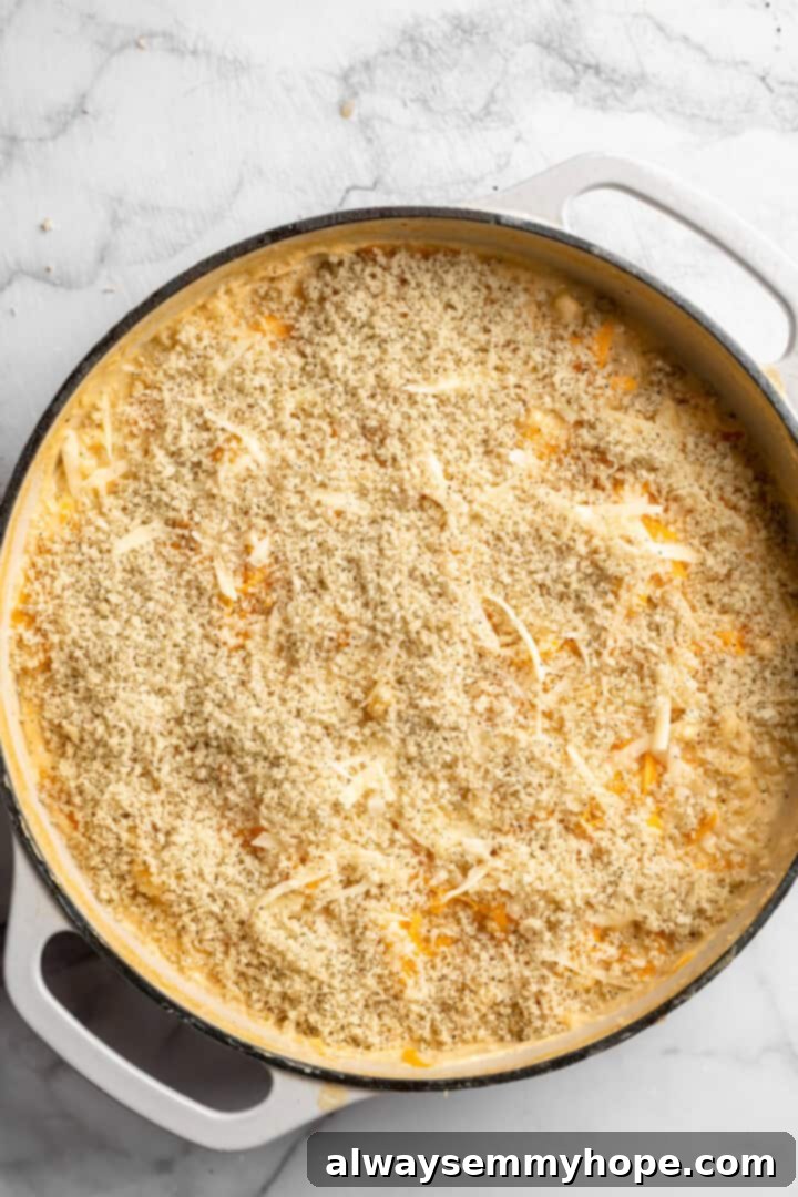 A generous layer of seasoned panko bread crumbs sprinkled over the creamy 3-Cheese Vegan Mac and Cheese in a skillet, ready for baking.