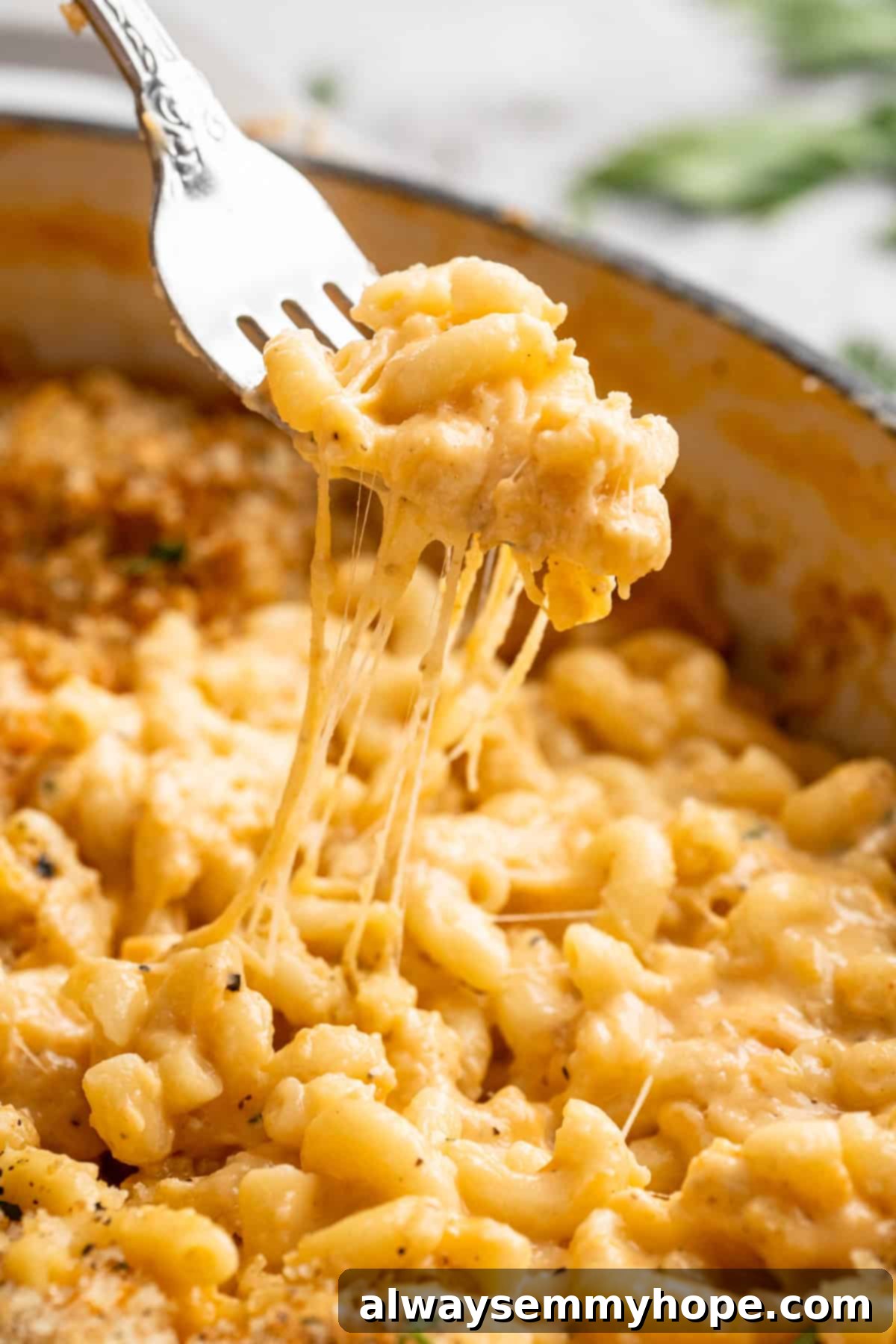 A fork lifts a generous, gooey portion of 3-Cheese Vegan Mac and Cheese from a skillet, showing off the perfect cheese pull and crispy panko topping.