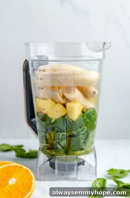 This vegan green smoothie only has four ingredients and is one of my favourite quick, easy breakfasts. It's smooth and creamy without dairy! Green smoothie ingredients in a blender before being blended, showing pineapple, spinach, bananas, and orange juice.