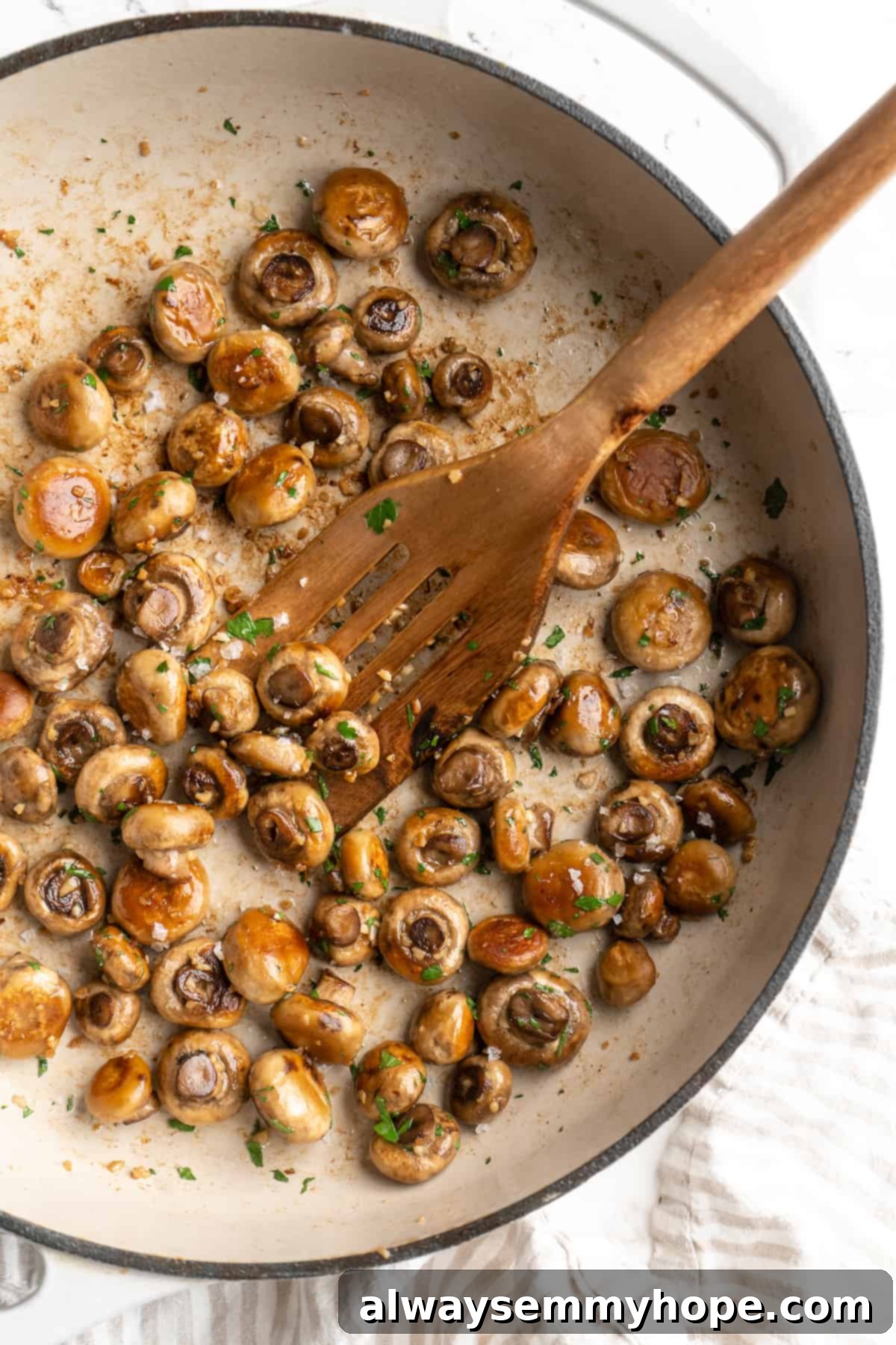 Overhead view of garlic mushrooms in skillet with spatula