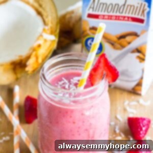 Strawberry coconut smoothie in a mason jar wit a straw and strawberries.