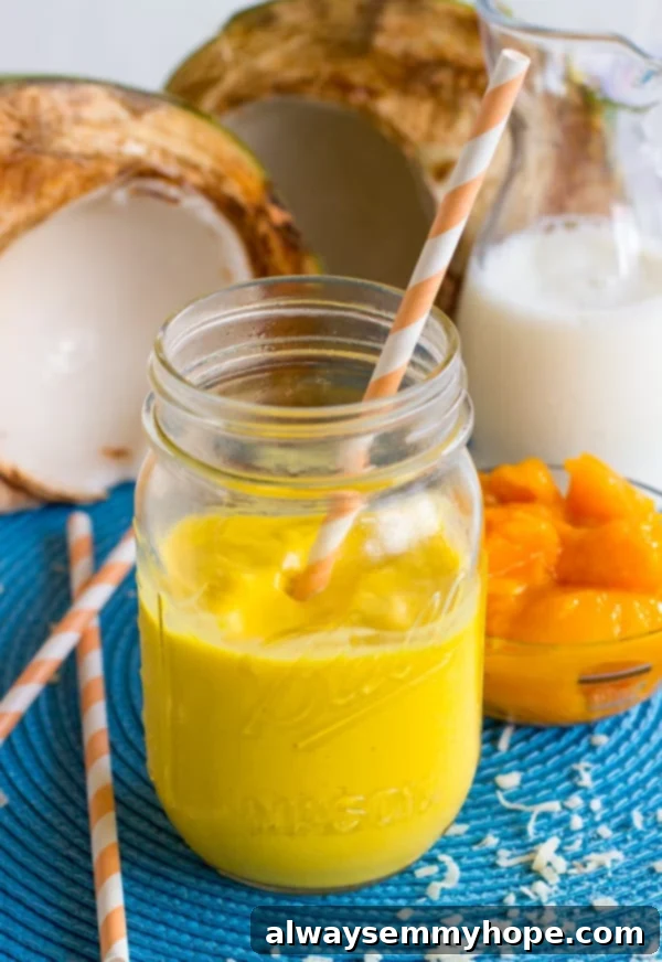 Vibrant Mango Coconut Smoothie served in a clear mason jar with a yellow straw, garnished with a fresh mango slice on the rim.