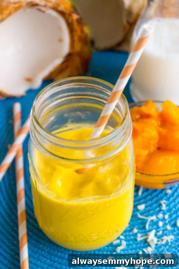 Close-up shot of the incredibly smooth and vibrant Mango Coconut Smoothie in a mason jar, highlighting its creamy texture and rich color, with a yellow reusable straw.