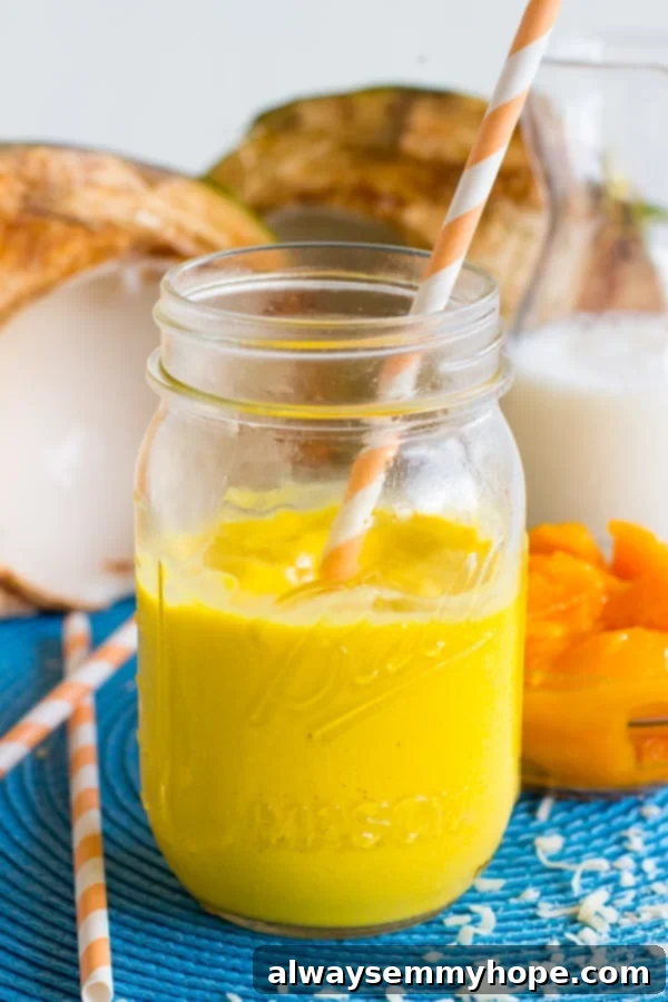 Side view of the creamy Mango Coconut Smoothie presented in a clear glass mason jar, highlighting its beautiful yellow hue and smooth consistency.