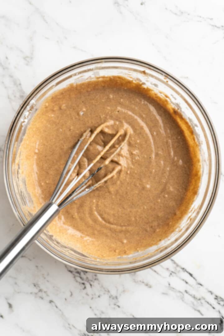 Overhead close-up of a mixing bowl containing a smooth, creamy pumpkin pancake batter with a whisk resting in it, showing the final consistency before cooking.