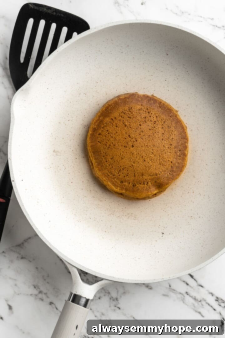 Overhead close-up of a single golden-brown vegan pumpkin pancake, perfectly cooked and lightly browned, resting in a hot pan.