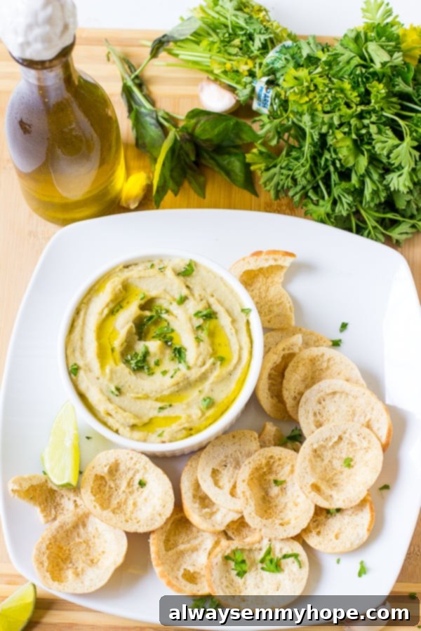Top down shot of herbed roasted garlic white bean dip in a white ramekin with chips on the side, inviting you to dip.
