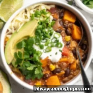 Overhead view of sweet potato and black bean chili in bowl with cashew sour cream, avocado, cilantro, and green onion