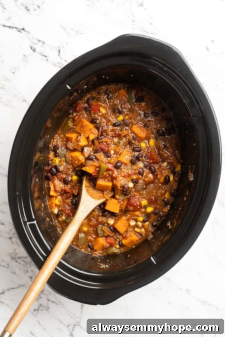 Overhead view of vegan sweet potato and black bean chili in slow cooker insert with wooden spoon