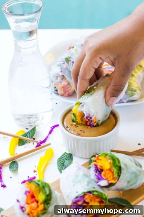 A hand gracefully dipping a fresh summer roll into a bowl of rich peanut sauce, illustrating the ultimate way to enjoy this delicious appetizer or meal.