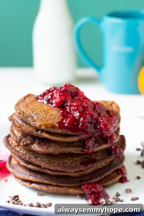 Chocolate peanut butter pancakes generously covered in a luscious raspberry compote, resting on a white plate, ready to be served.