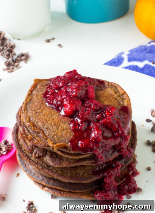 An overhead shot showcasing a platter of chocolate peanut butter pancakes topped with fresh berries and a generous drizzle of raspberry compote, ready to serve.