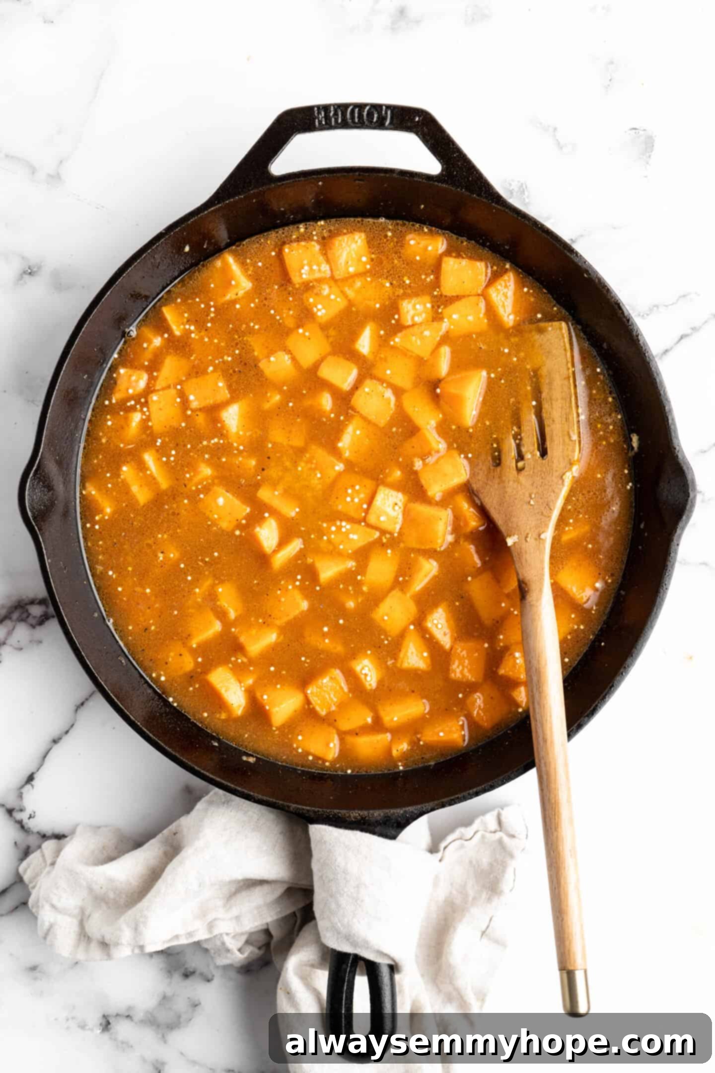 Sweet potatoes and uncooked quinoa simmering in a savory vegetable broth with spices in a skillet, absorbing the liquid and flavors.