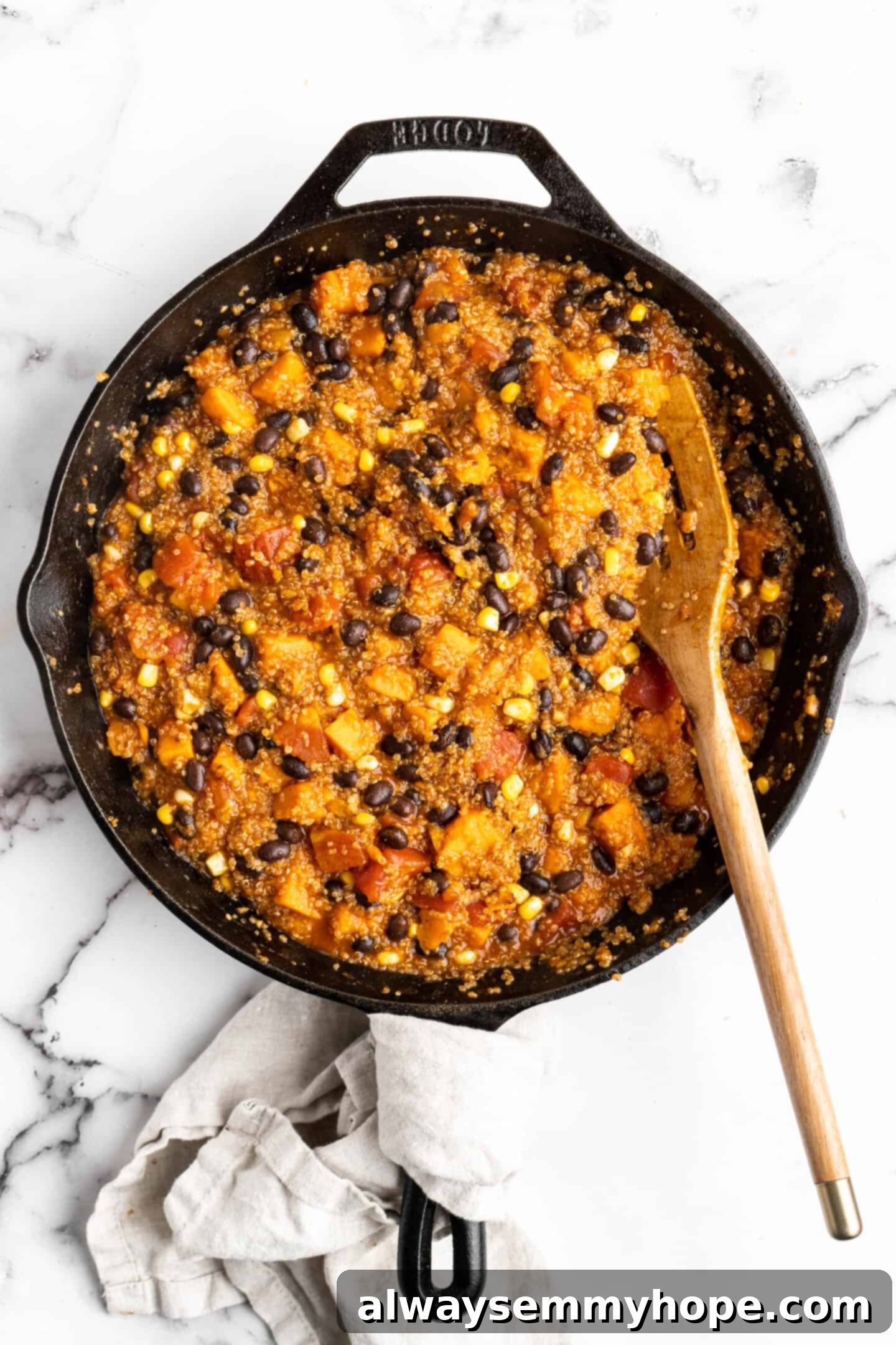 A vibrant vegan enchilada skillet, fully cooked with black beans, corn, and tomatoes mixed in, ready for cheese and final garnishes.