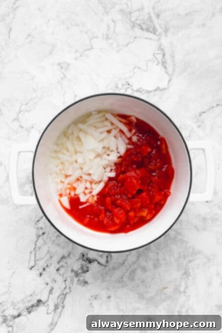 Diced onions and tomatoes simmering in a pot with coconut oil, beginning to soften.