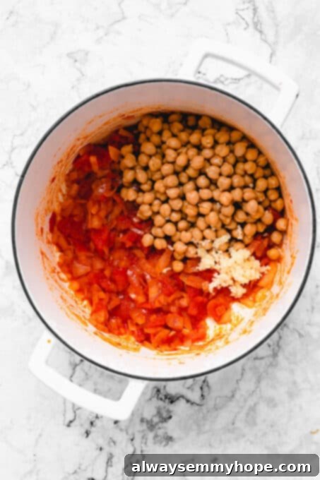 Chickpeas and spices added to the sautéed onions and tomatoes in a pot.