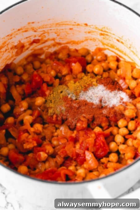 Close-up of chickpeas and spices being stirred into the curry base.