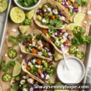 Overhead view of sweet potato and black bean tacos on parchment-lined baking sheet with toppings