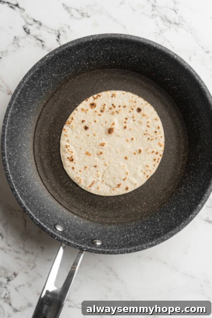 Overhead view of a tortilla warming in a skillet, showing slight browning and puffing, ready for assembly