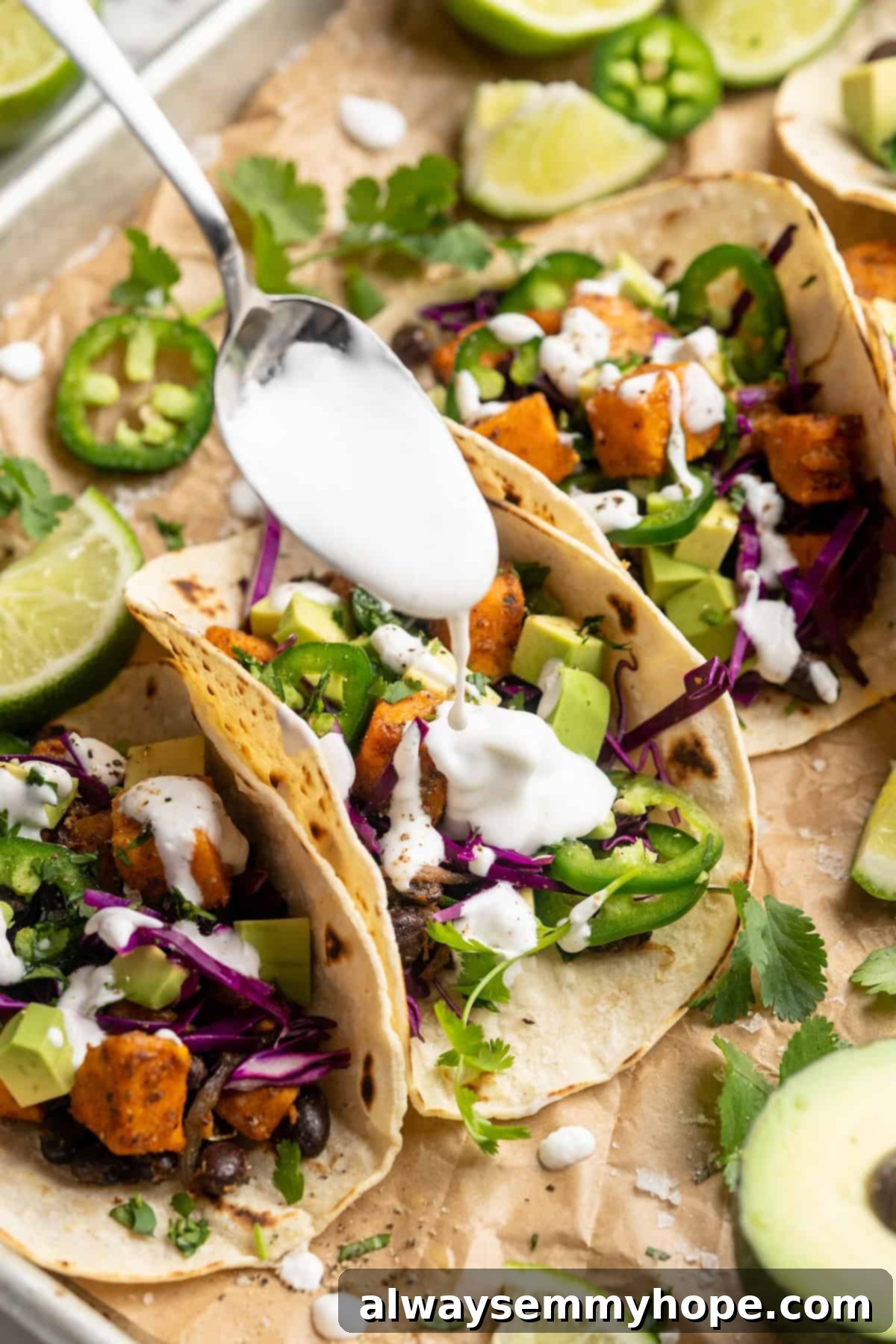Close-up shot of lime crema being drizzled over freshly assembled sweet potato and black bean tacos, creating an enticing visual