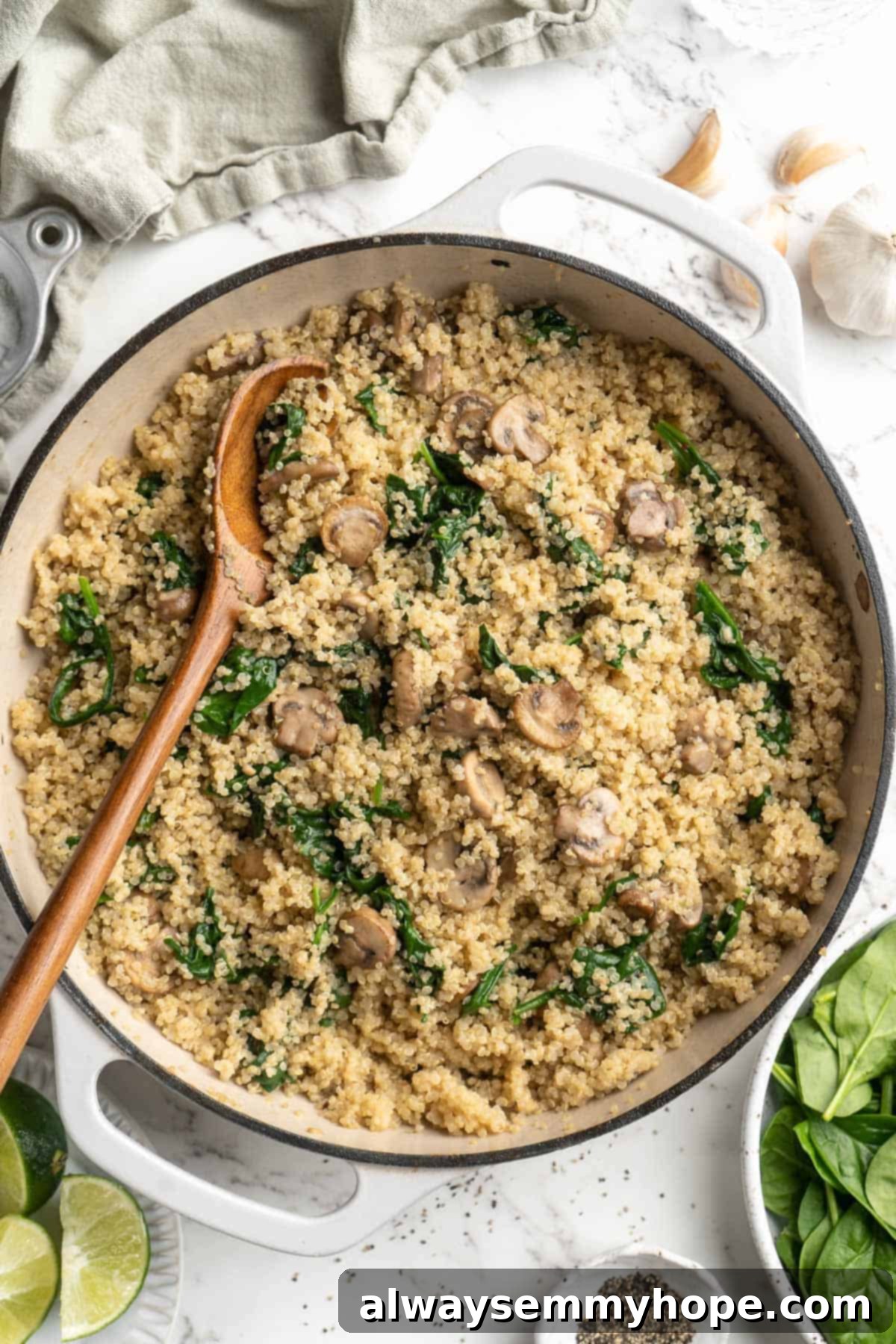 Overhead view of coconut creamy spinach and mushroom quinoa in skillet with wooden spoon, highlighting the rich texture and vibrant ingredients.
