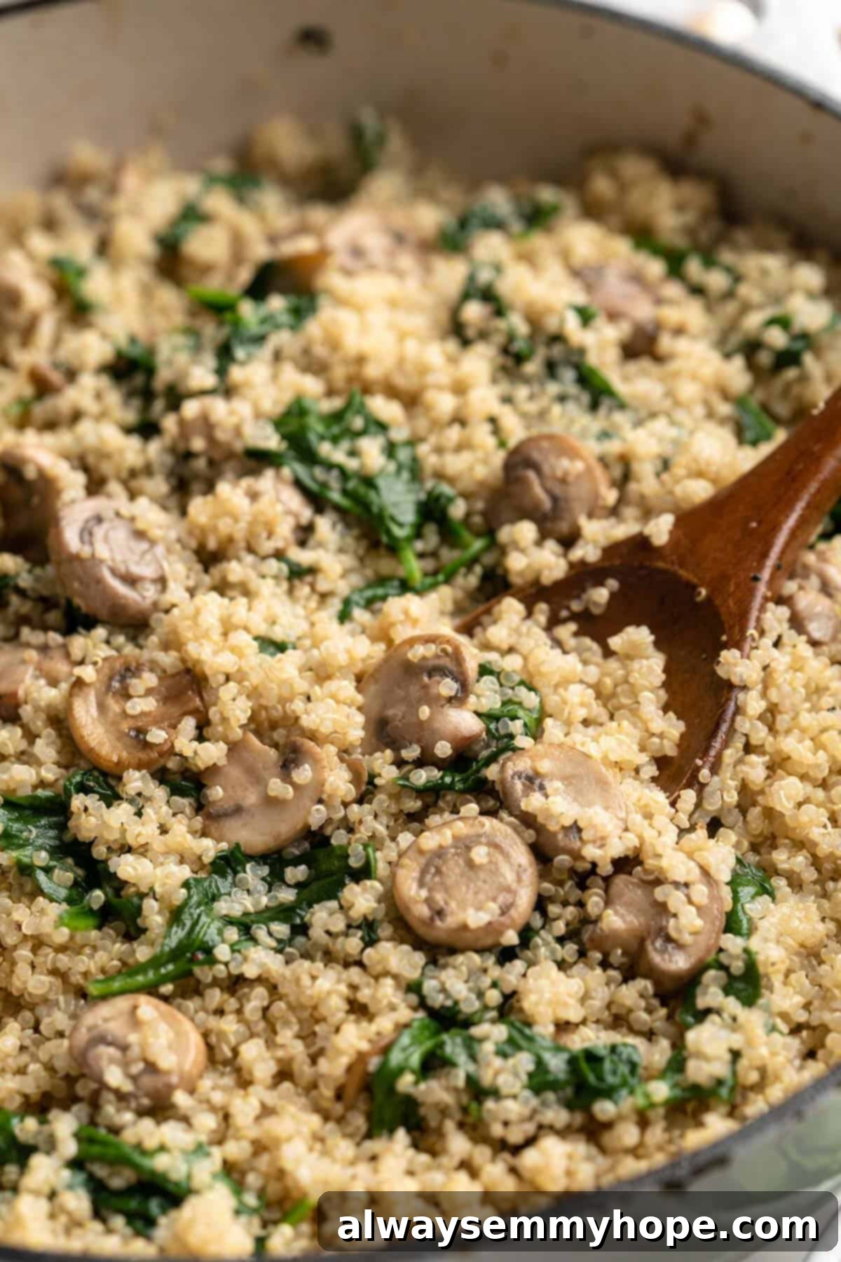 Close-up overhead view of the creamy coconut spinach and mushroom quinoa in a skillet with a wooden spoon, ready to be served into bowls.