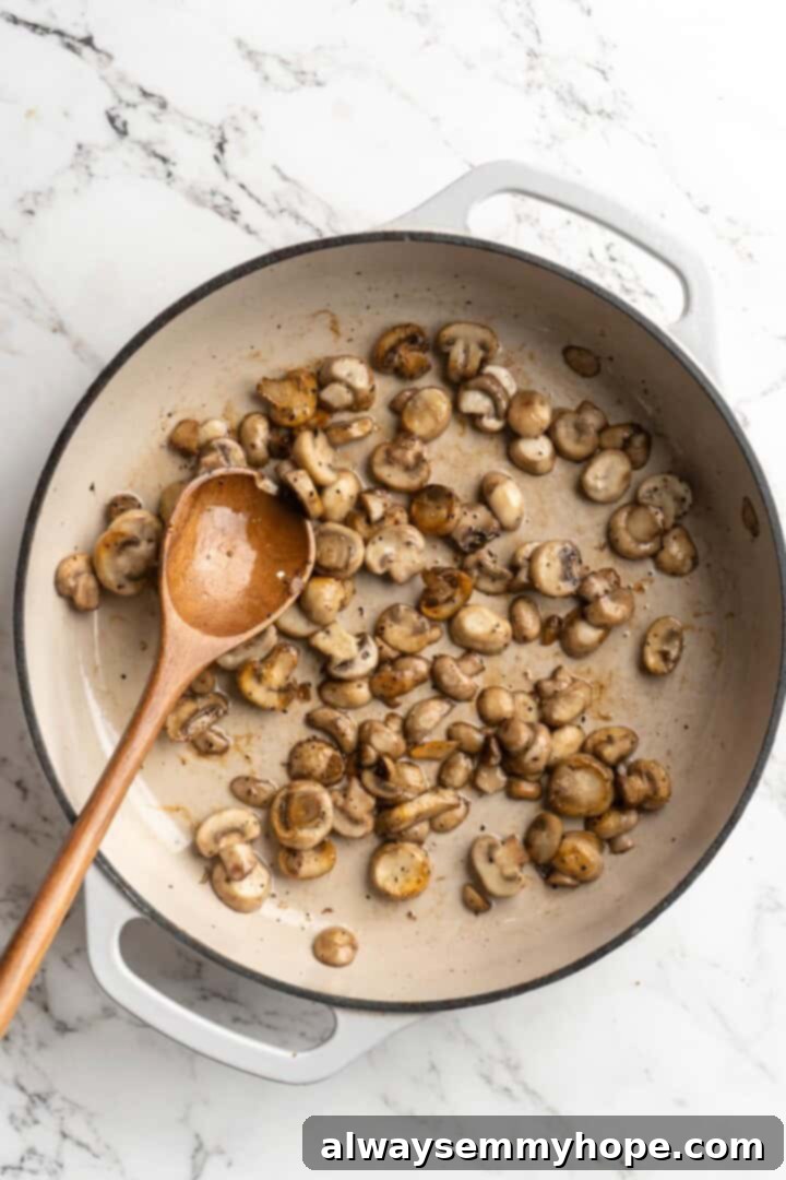 Overhead view of sliced mushrooms being sautéed in a skillet with olive oil, beginning to brown.