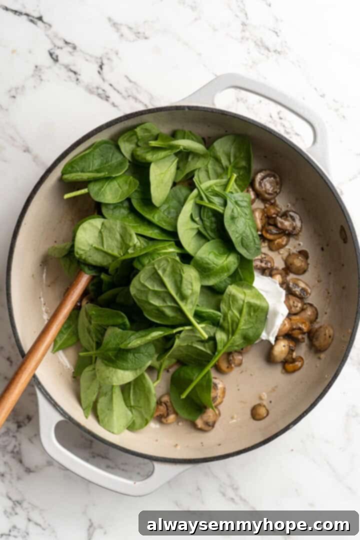 Overhead view of fresh raw spinach being added to the skillet with sautéed mushrooms.