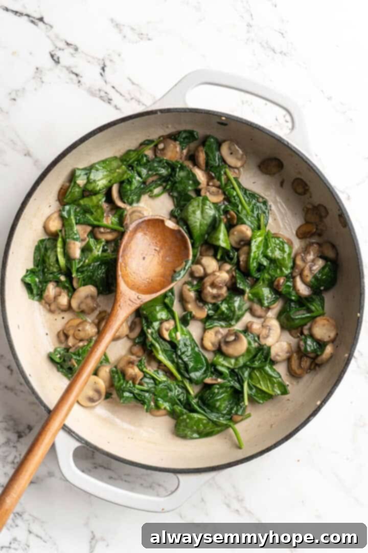 Overhead view of wilted spinach and cooked mushrooms combined in a skillet, creating a vibrant mixture.