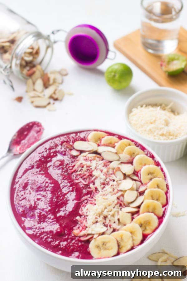 Banana berry beet smoothie bowl on a white table top with ingredients around it. 