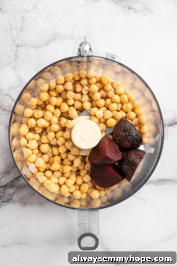 Step 1: Pulse roasted beets and chickpeas in a food processor until roughly combined for your beet hummus. Roasted beets and chickpeas pulsed together in a food processor bowl, creating a coarse, pink mixture.