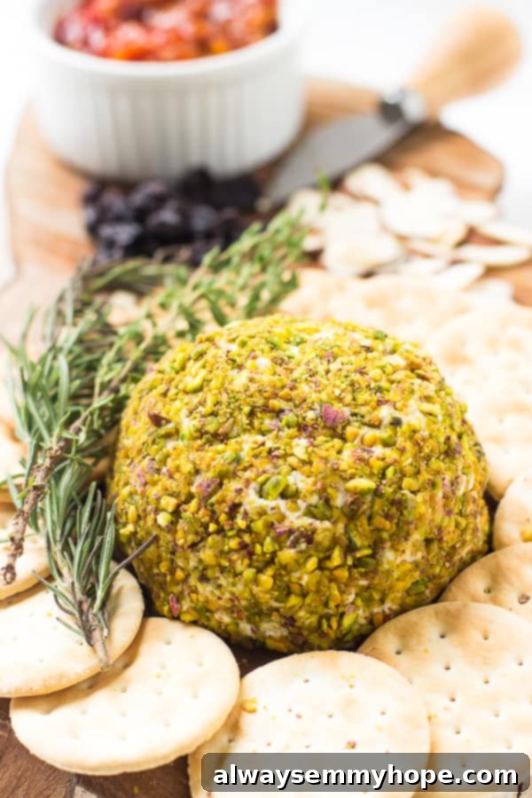 Pistachio Crowned Vegan Cheese Ball 5 Pistachio crusted vegan cheese ball on a cheese board with crackers and a sprig of rosemary.
