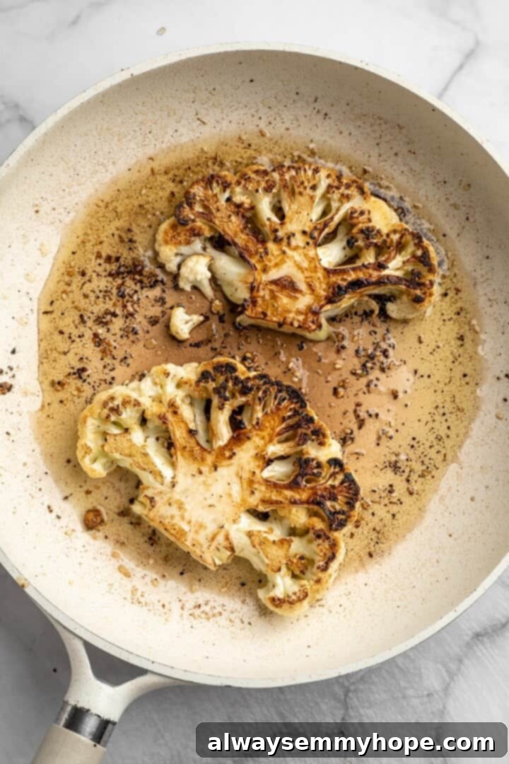 These easy roasted cauliflower steaks are tender, crispy on the edges, and incredibly flavourful thanks to the addition of za’atar! Overhead view of cauliflower steaks being seared in pan
