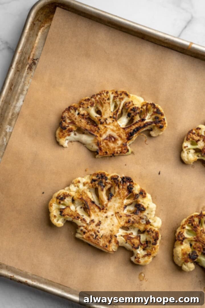 These easy roasted cauliflower steaks are tender, crispy on the edges, and incredibly flavourful thanks to the addition of za’atar! Overhead view of roasted cauliflower steaks on parchment-lined pan