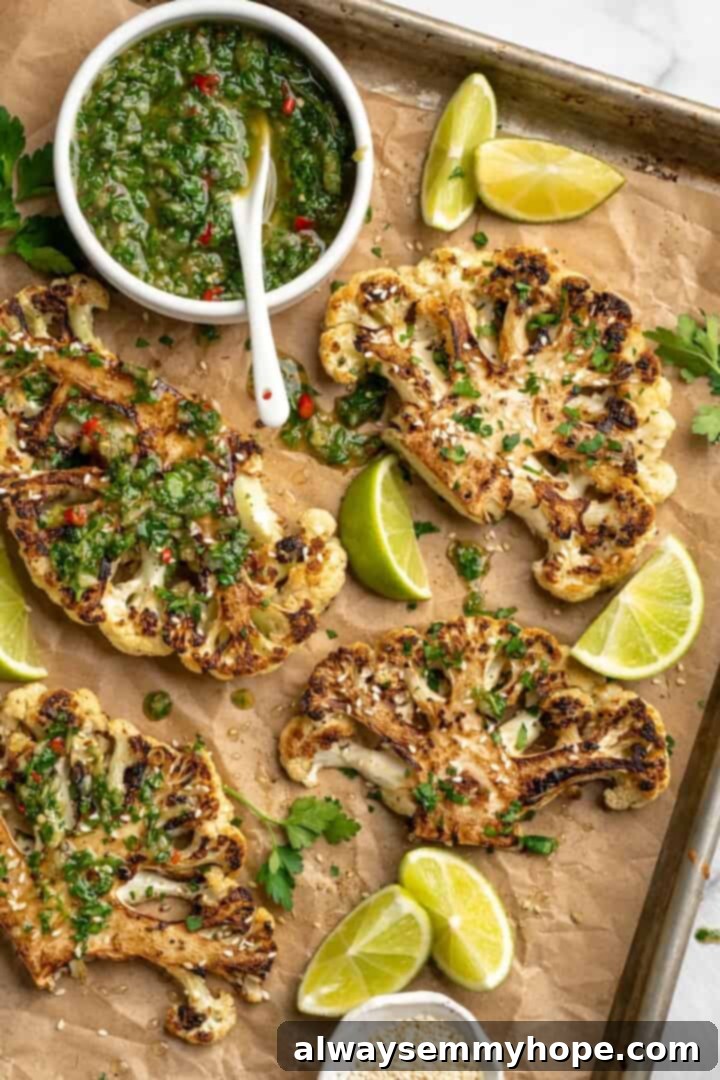 These easy roasted cauliflower steaks are tender, crispy on the edges, and incredibly flavourful thanks to the addition of za’atar! Overhead view of cauliflower steaks on sheet pan with chimichurri in bowl