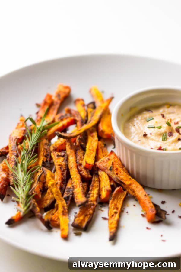 Crispy baked carrot fries on a white plate with a ramekin of harissa tahini dip on the side.