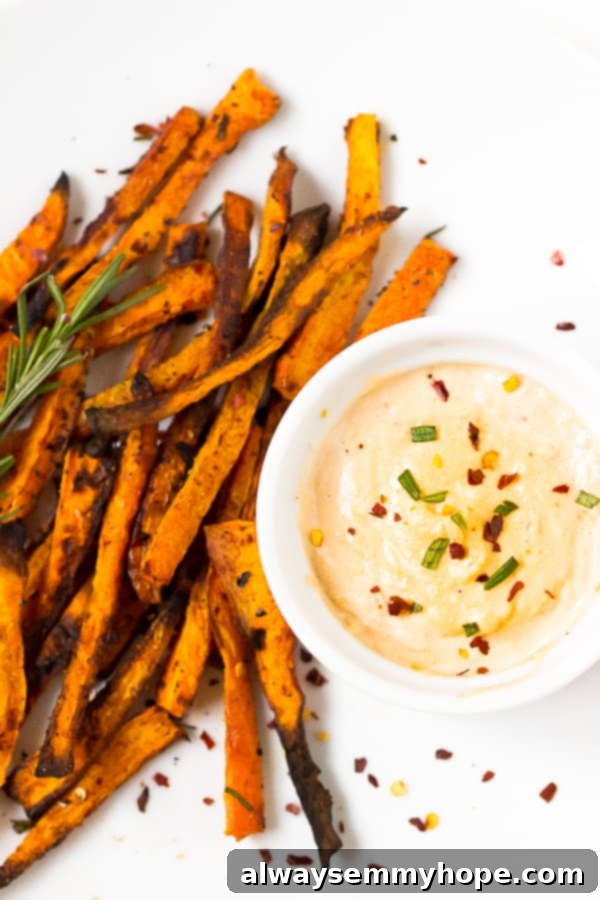 Top-down view of golden crispy baked carrot fries arranged on a white plate with a small bowl of harissa tahini dip.