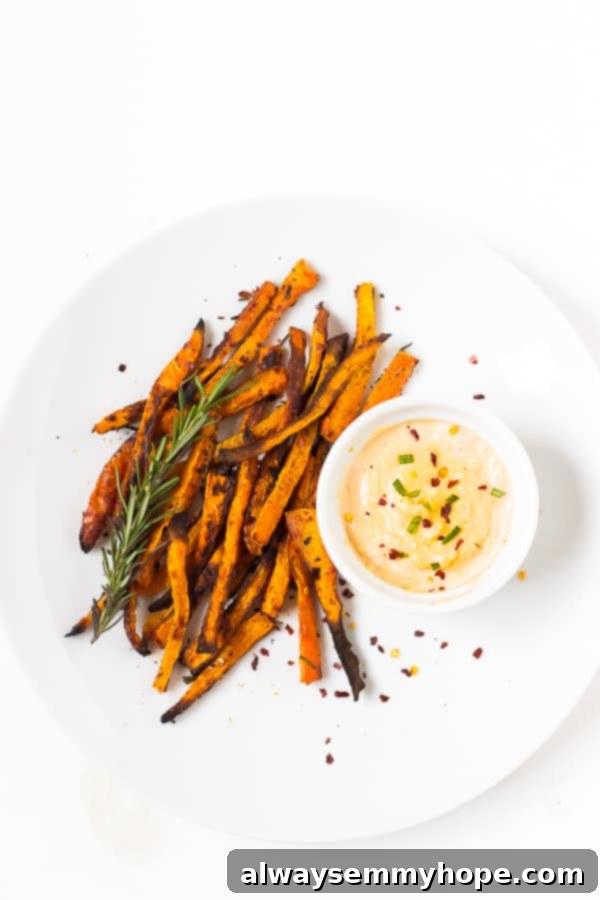 Overhead shot of crispy baked carrot fries on a white backdrop, perfectly golden, with a small ramekin of harissa tahini dip.