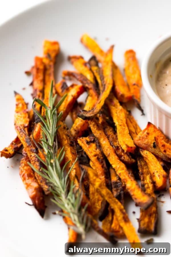 Crispy baked carrot fries on a white plate with a sprig of fresh rosemary garnish.