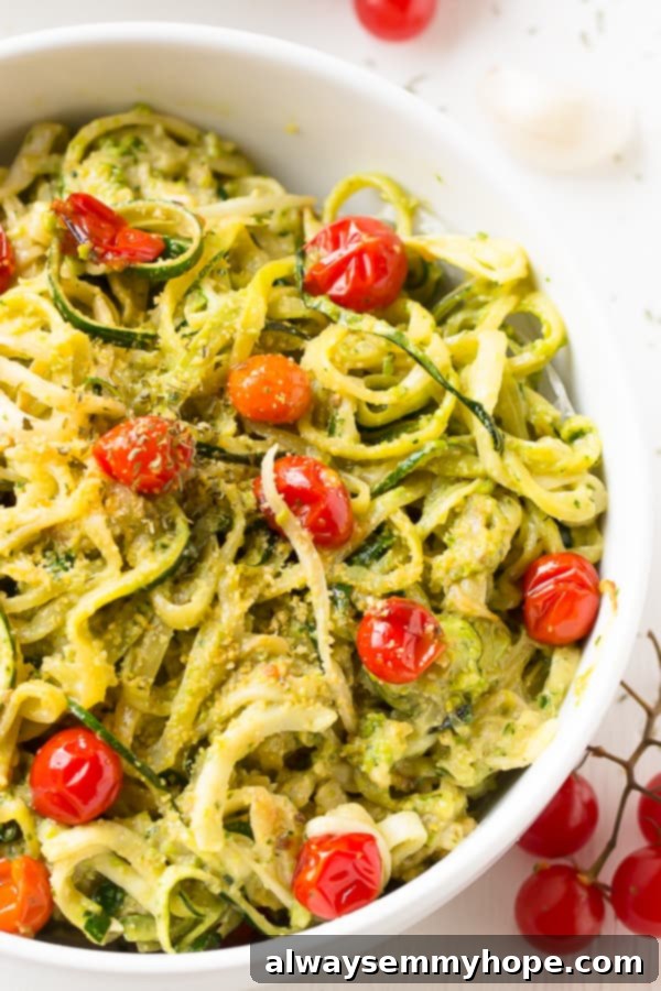 Zucchini Noodles with Pesto and Burst Cherry Tomatoes 3 Pesto zucchini noodles with burst cherry tomatoes in a white bowl, with fresh cherry tomatoes on the side, highlighting the dish's vibrant ingredients.