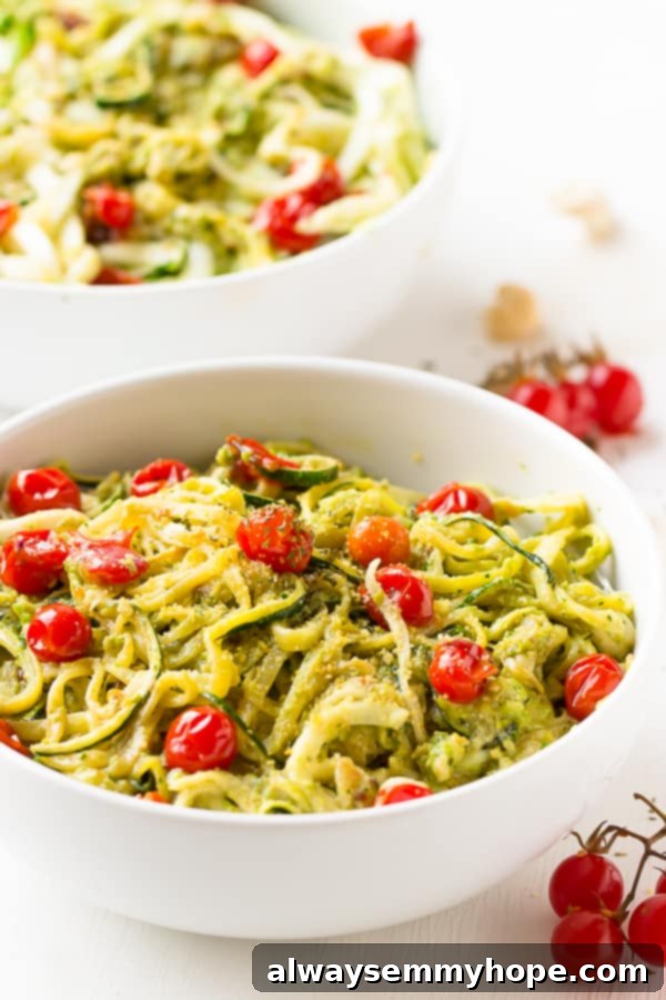 Zucchini Noodles with Pesto and Burst Cherry Tomatoes 5 Two white bowls of pesto zucchini noodles and burst cherry tomatoes, beautifully presented on a clean white table, ready to be served.
