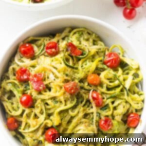 Zucchini Noodles with Pesto and Burst Cherry Tomatoes 7 Overhead shot of pesto zucchini noodles in a big white bowl, garnished with fresh herbs and a fork.
