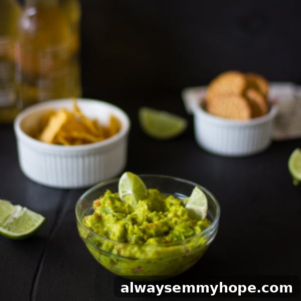 Spicy guacamole in a glass bowl with chips in the background. 