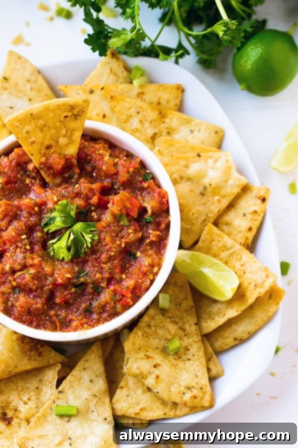 This easy restaurant-style blender salsa is made with fresh tomatoes for lots of bright flavour. Add your fave tortilla chips and dig in! Top down shot of salsa in a white ramekin with chips around it.