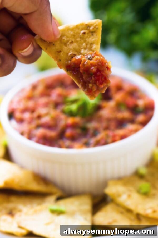 This easy restaurant-style blender salsa is made with fresh tomatoes for lots of bright flavour. Add your fave tortilla chips and dig in! Hand holding tortilla chip with restaurant-style blender salsa