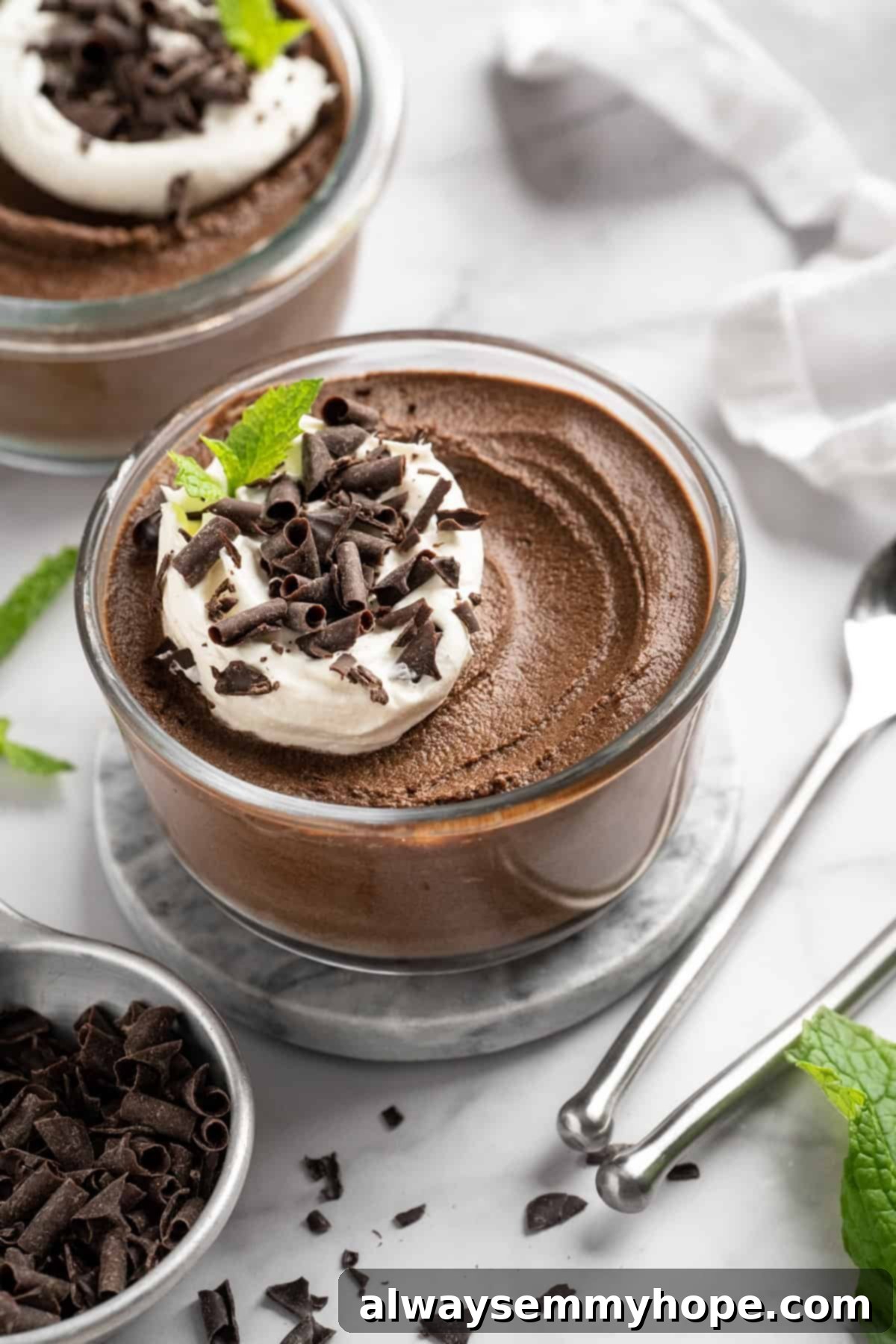 This Chocolate Avocado Pudding is ultra rich and decadent, with the creamiest texture and deepest chocolate flavour. Just 10 minutes of prep! A beautifully presented bowl of creamy chocolate avocado pudding, generously topped with fluffy coconut whipped cream and delicate chocolate shavings, inviting you to take a spoonful.