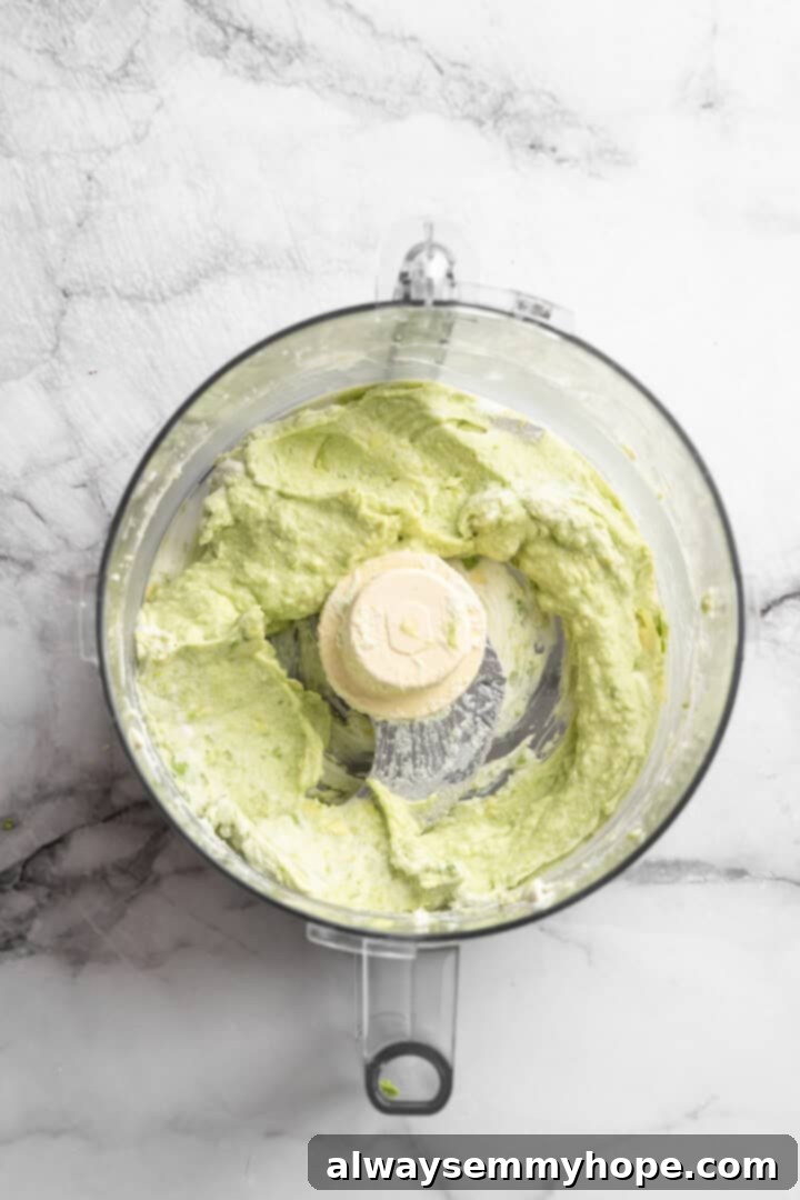 This Chocolate Avocado Pudding is ultra rich and decadent, with the creamiest texture and deepest chocolate flavour. Just 10 minutes of prep! Halved ripe avocado and thick white coconut cream are shown blended together in a food processor, creating a smooth, pale green base for the pudding.