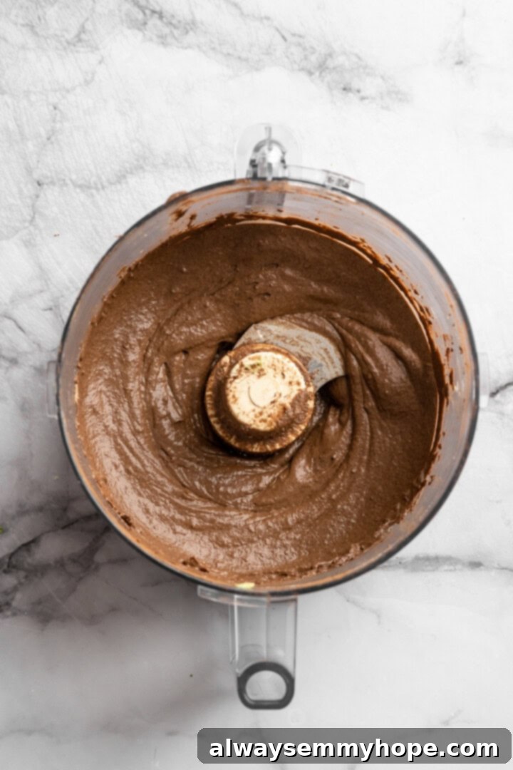 This Chocolate Avocado Pudding is ultra rich and decadent, with the creamiest texture and deepest chocolate flavour. Just 10 minutes of prep! The food processor now contains a dark brown, smooth mixture, indicating that the banana, maple syrup, and cocoa powder have been added and fully blended into the avocado base.